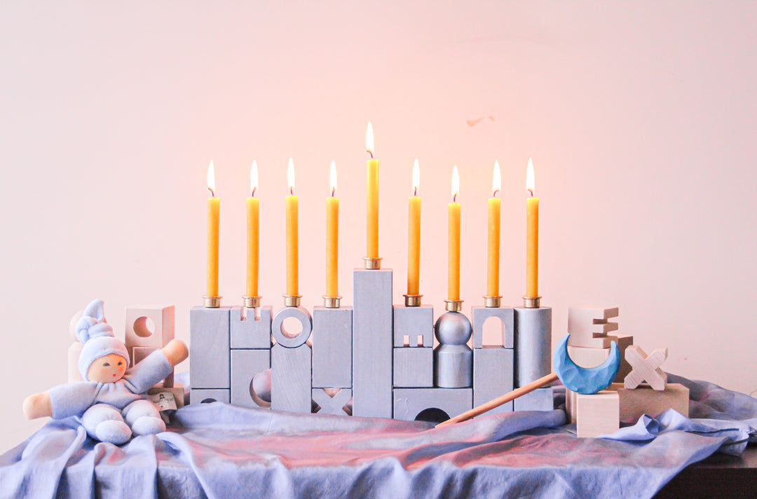 A HABA Block Menorah sits on a playsilk with lit candles.