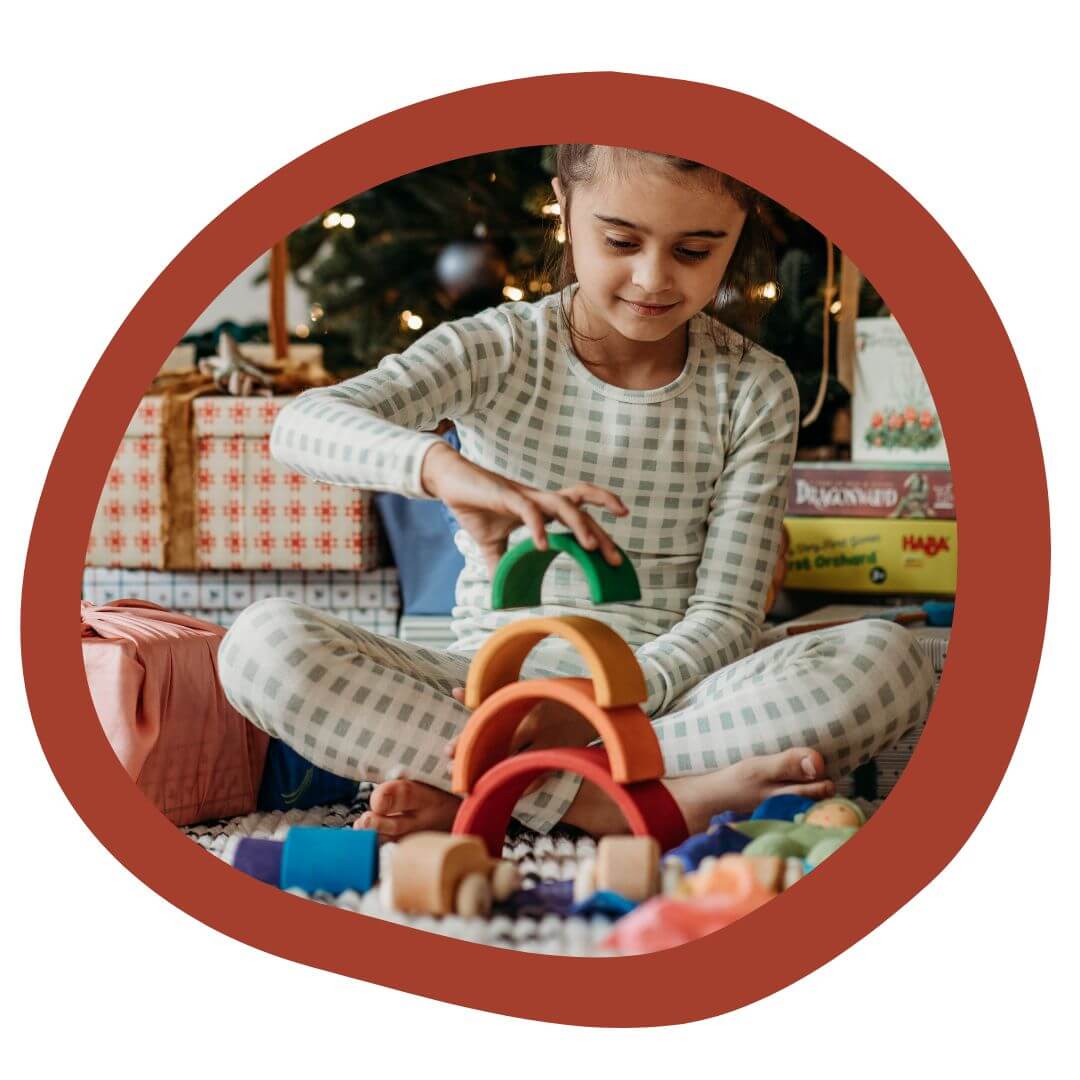 Child playing with Grimm's Wooden Rainbow in front of Christmas tree