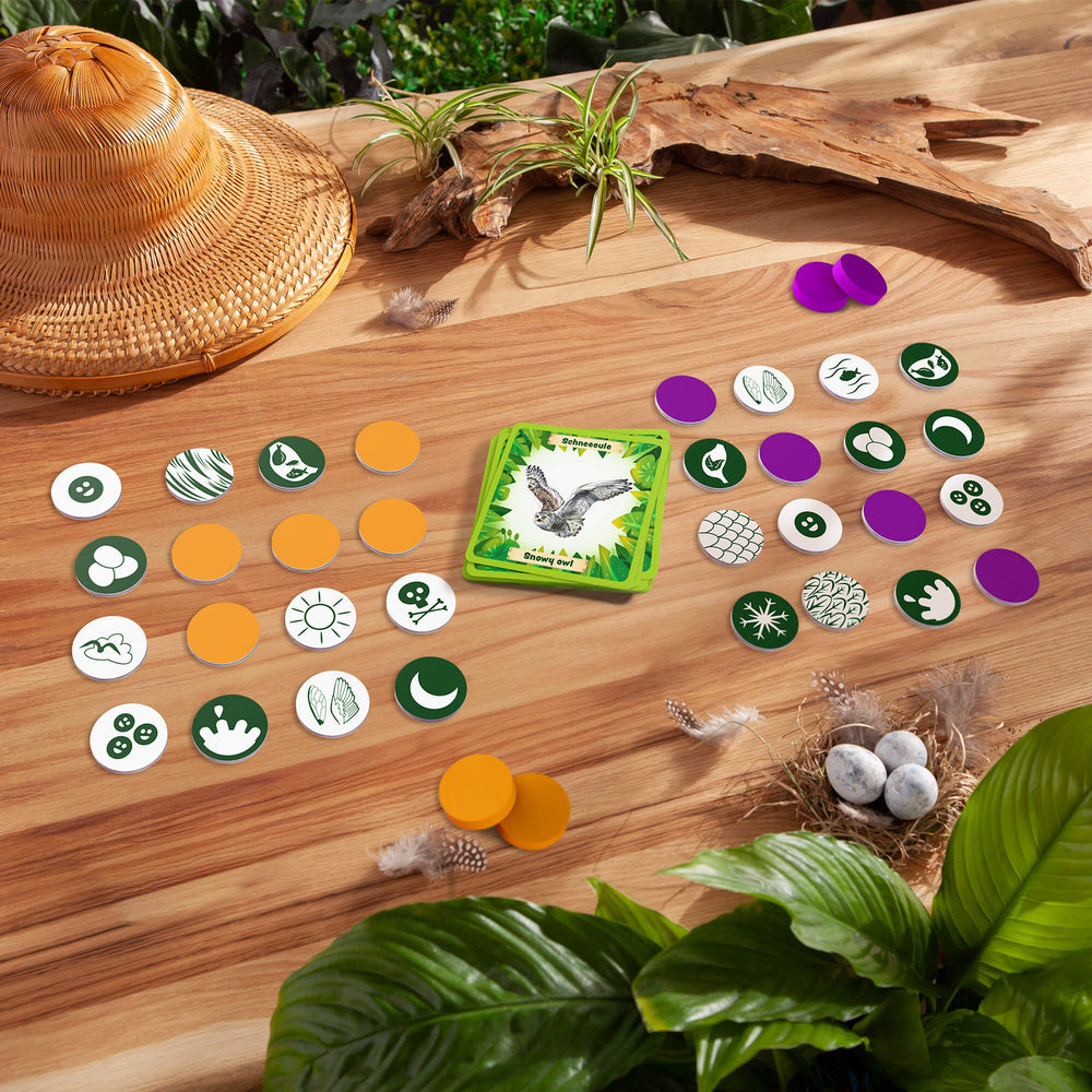 HABA Animals of the World Bingo Board game components on a wooden surface with plants and a hat.