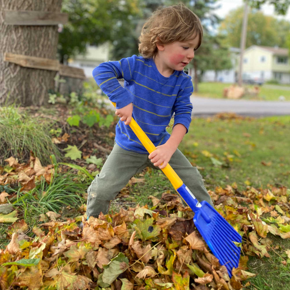 Child in blue shirt and green pants raking leaves with Spielstabil Long Handled Leaf Rake