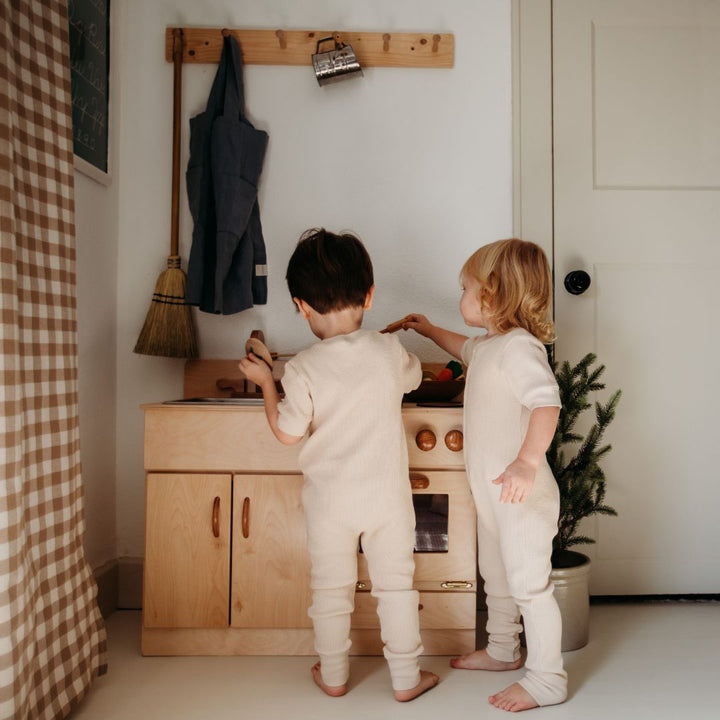 Bella Luna Toys- Wooden Toys- Children in white pijamas playing with wooden kitchen in play corner