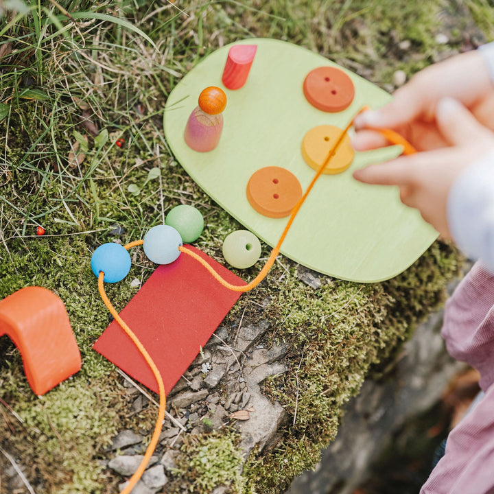 Grimms Down by the Meadow- Wooden Small World Play Set-Child threading wooden beads into orange string-Wooden Toys- Bella Luna Toys