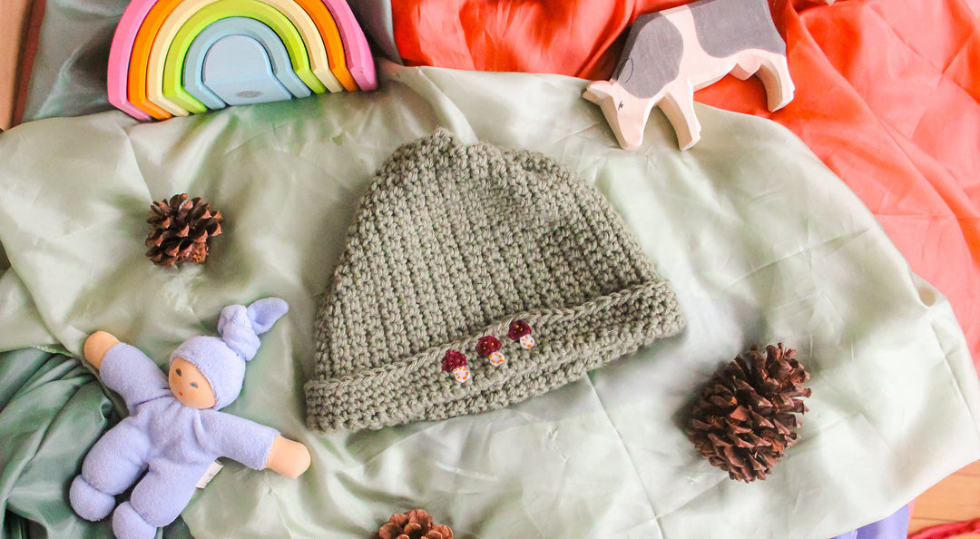 A simple green crochet hat sits next to Waldorf toys and playsilks.
