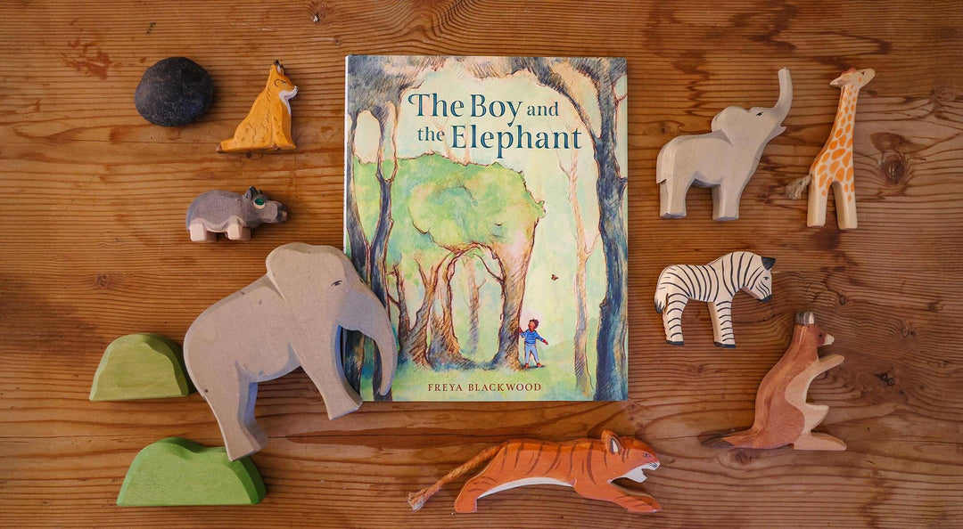 The boy and the elephant book on a table with wooden animals.