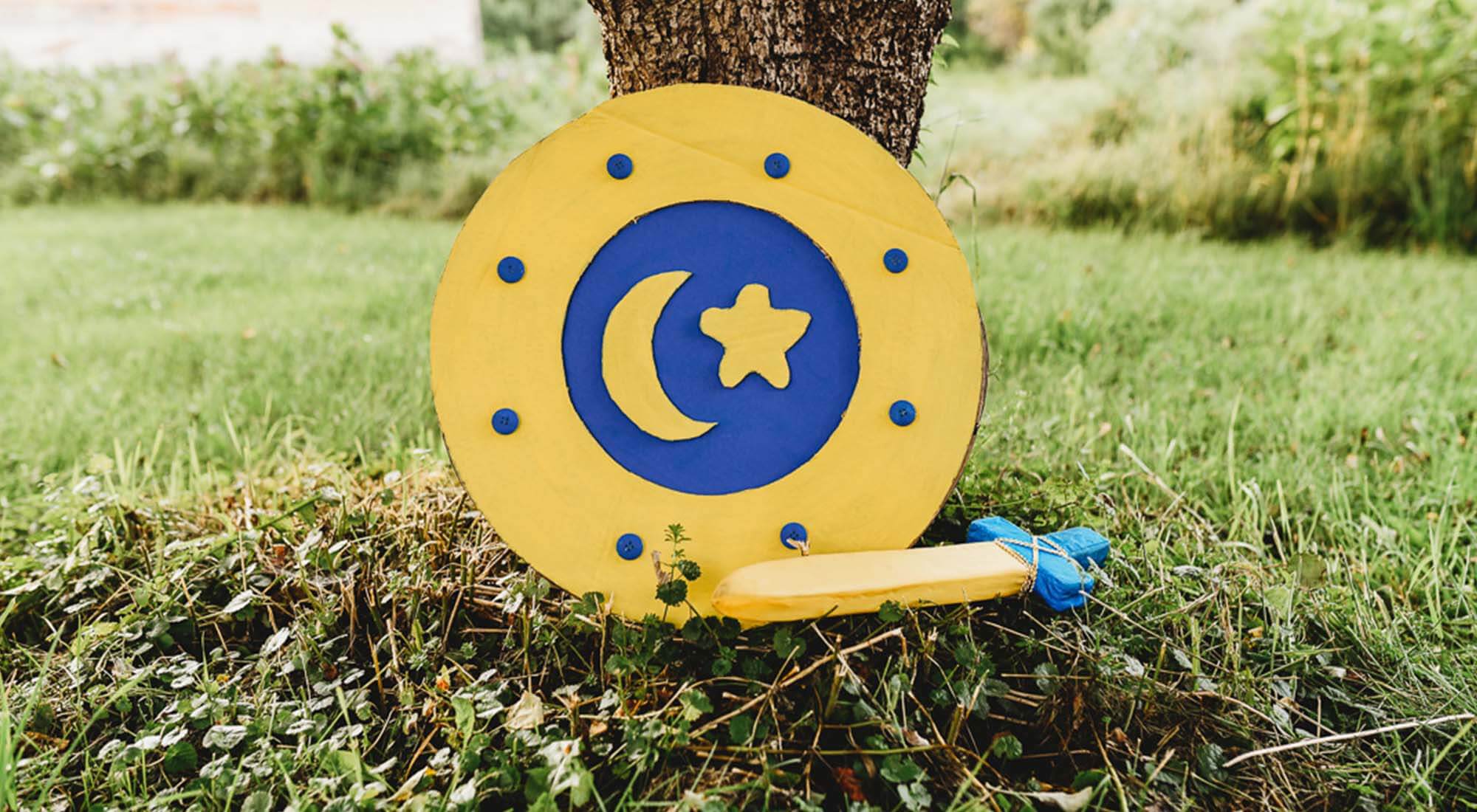 A cardboard knight shield in front of a tree.