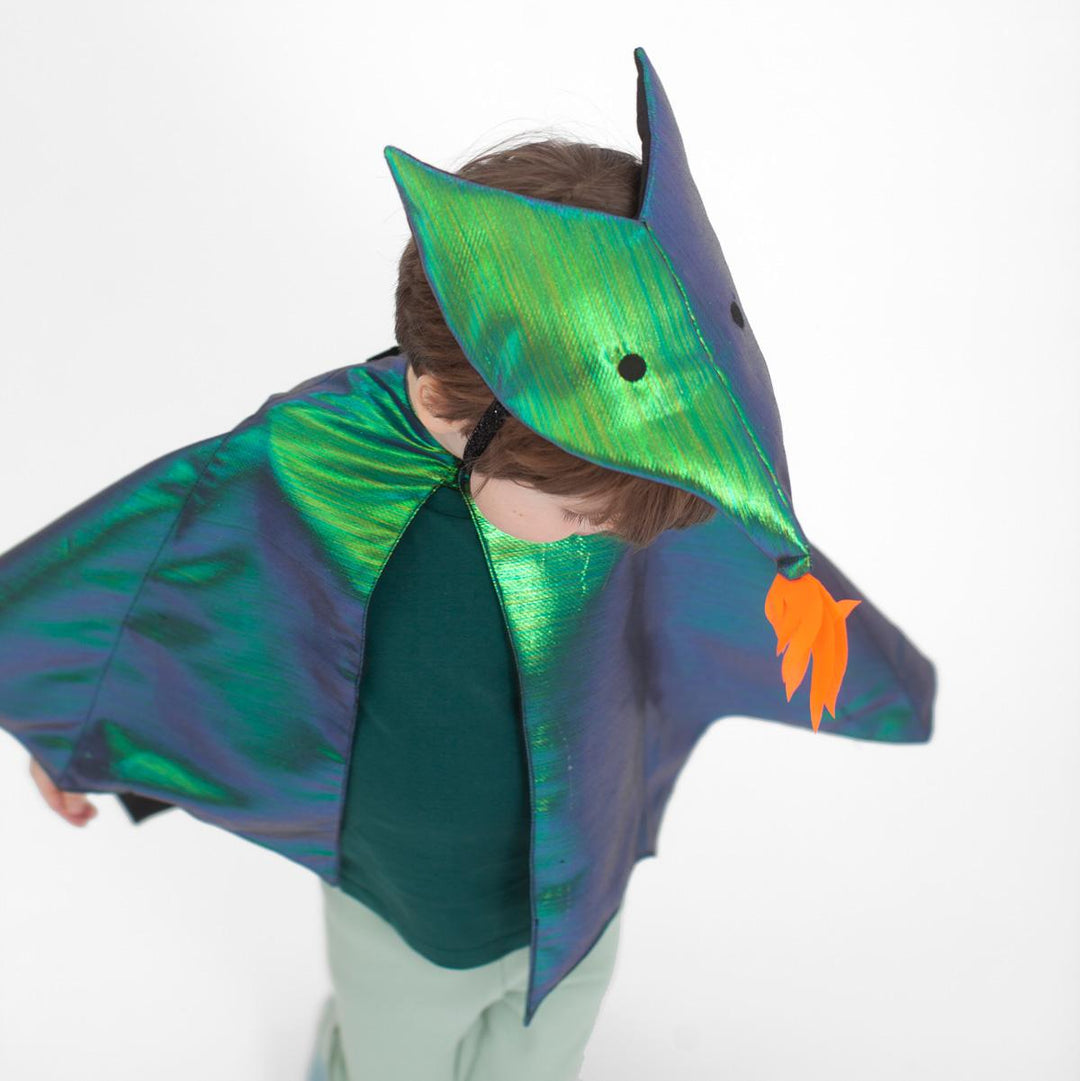 A view from above of a child wearing the green metallic dragon costume set from Meri Meri with winged cape and dragon headpiece featuring flame detail and embroidered eyes.