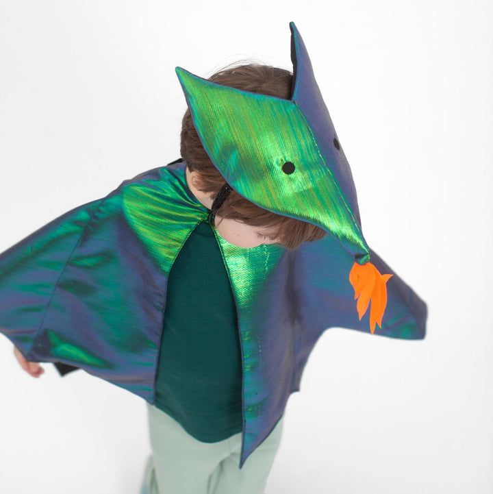 A view from above of a child wearing the green metallic dragon costume set from Meri Meri with winged cape and dragon headpiece featuring flame detail and embroidered eyes.
