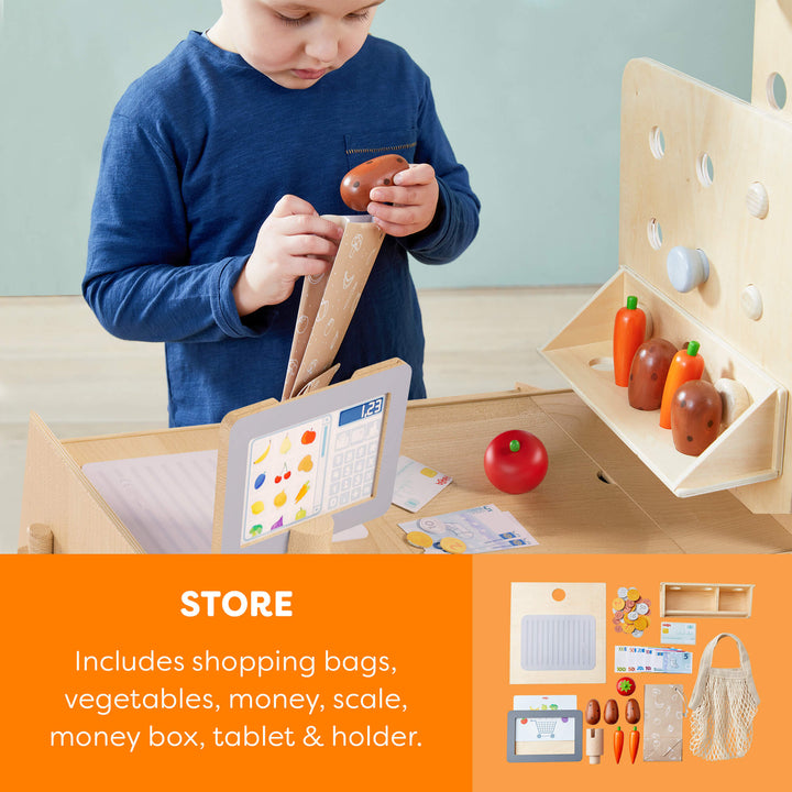 Child playing with a wooden toy set including vegetables, money, and a tablet holder.
