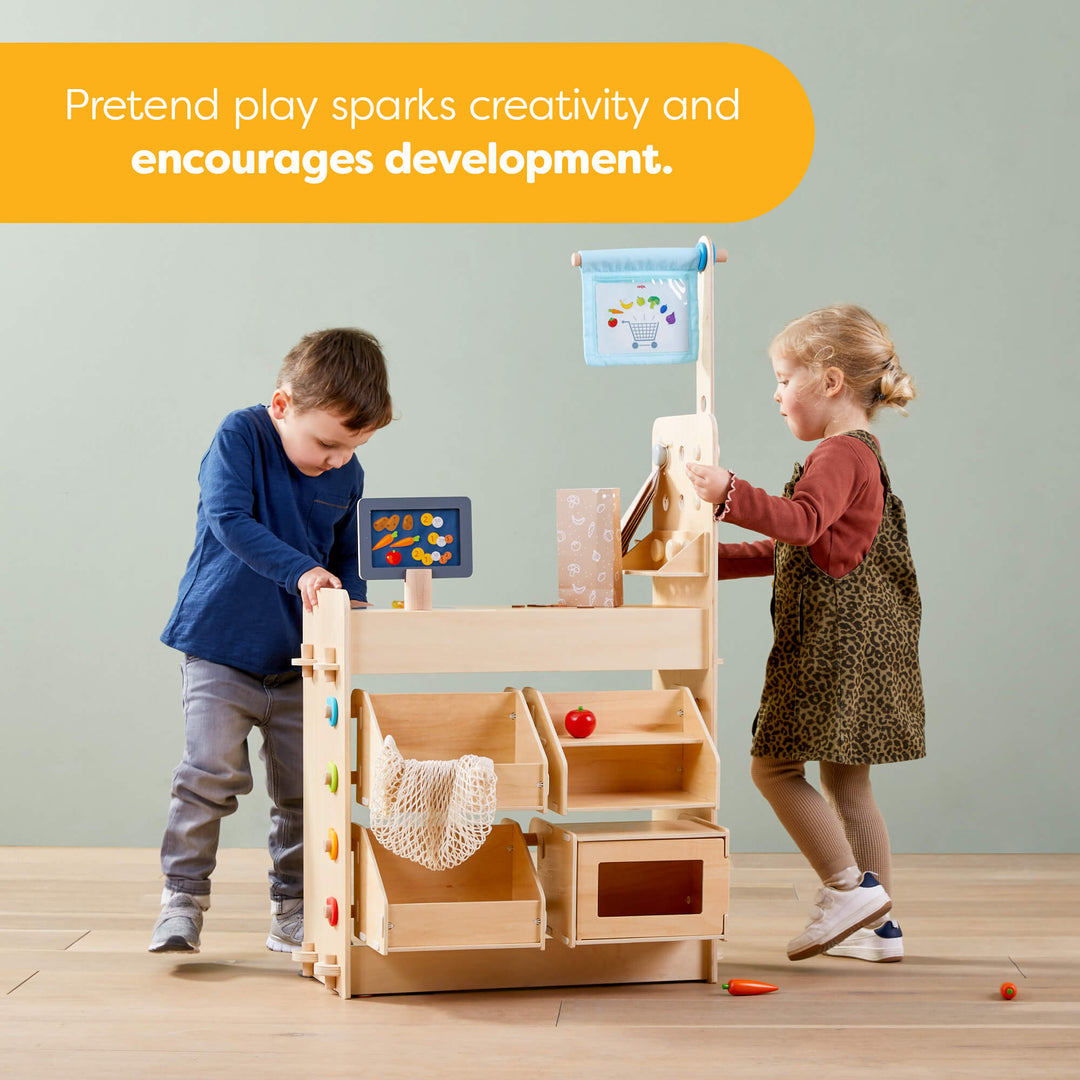 Two children playing with a wooden toy store set