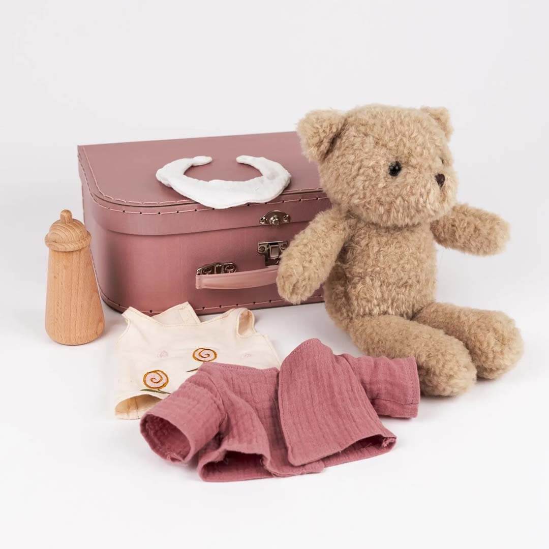 Teddy bear with a pink suitcase, clothes, and a bottle on a white background