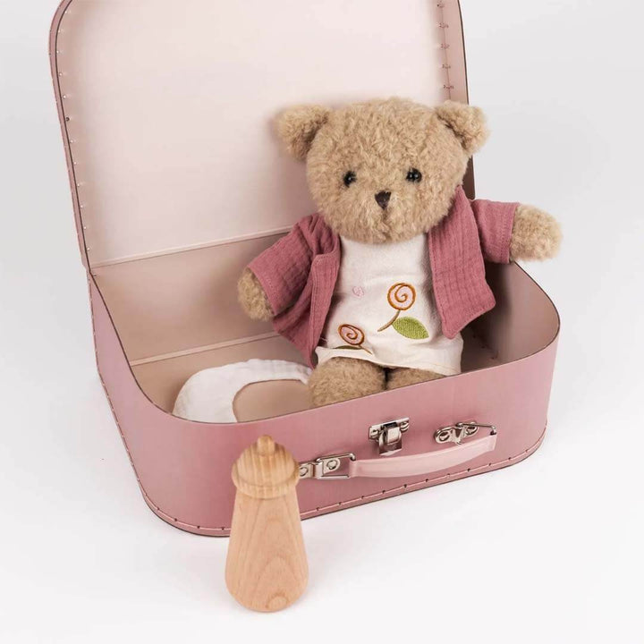 Teddy bear in a pink suitcase with a bottle on a white background