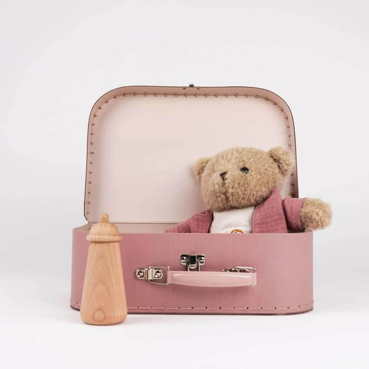 Small pink suitcase with a teddy bear and baby bottle on a white background