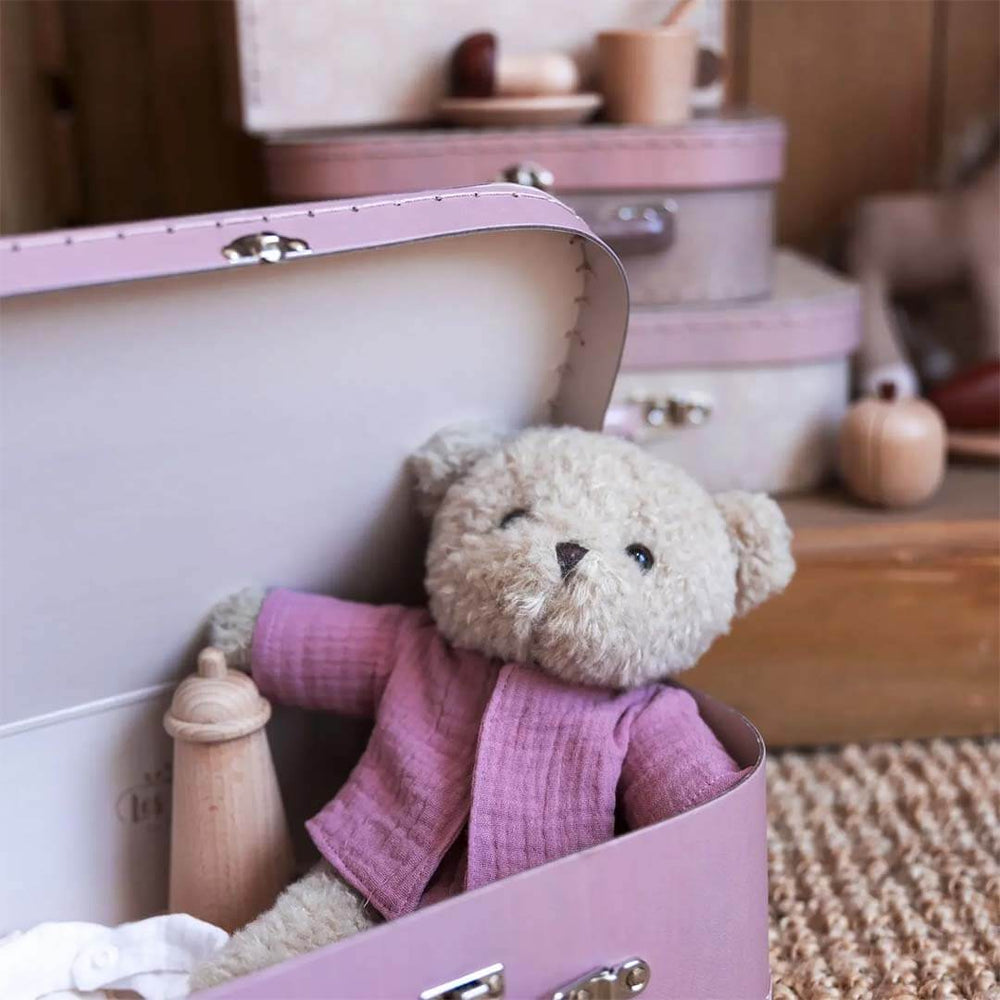 Teddy bear in a pink outfit sitting inside a pink suitcase with a blurred background