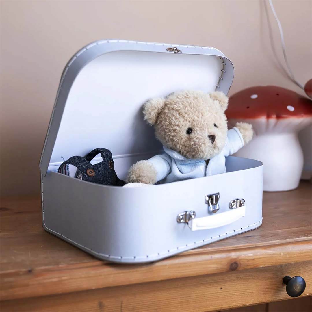 White suitcase with a teddy bear and black shoes on a wooden surface.