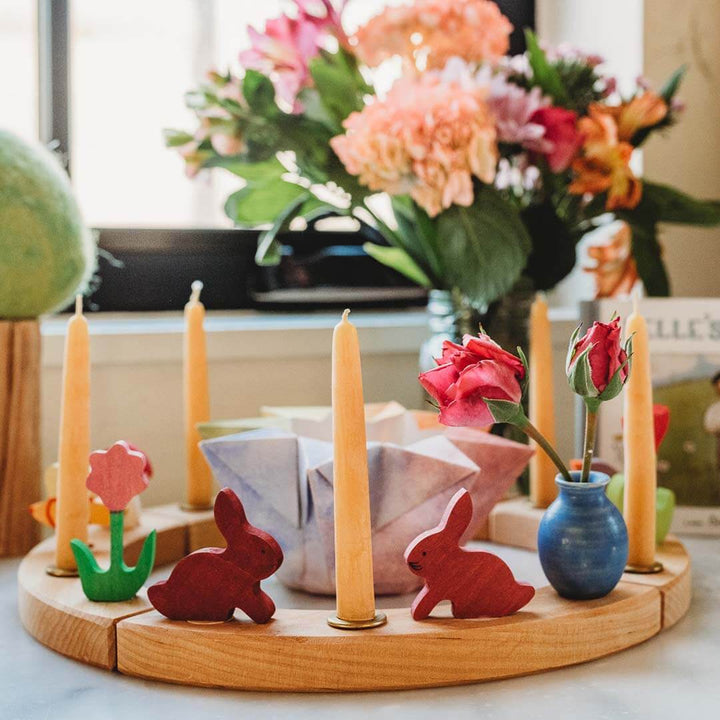 Decorative ring with candles, flowers, and wooden bunnies on a round wooden stand.