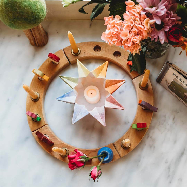 Wooden ring with colorful candles and a star-shaped candle on a marble surface with flowers.