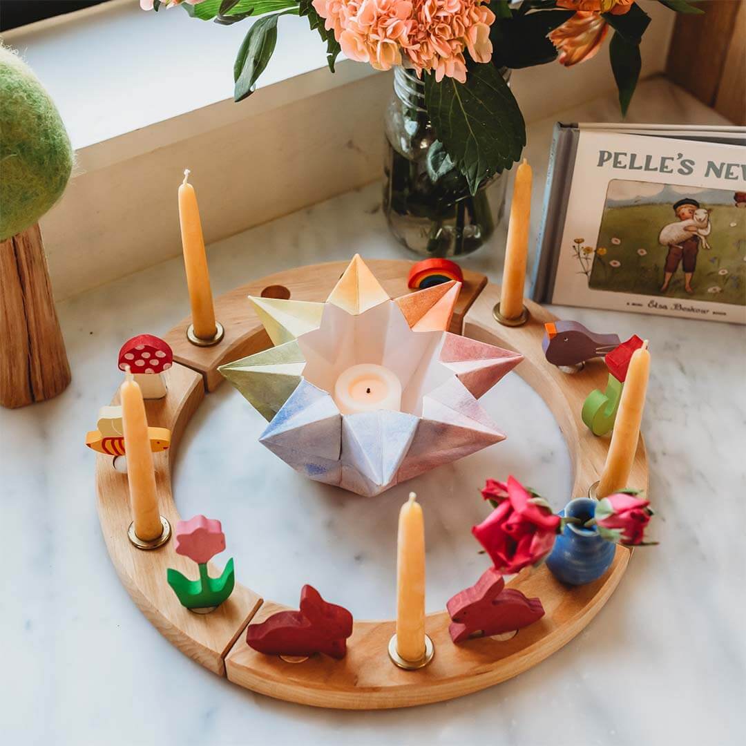 Wooden ring with candles and origami boat on a marble surface.