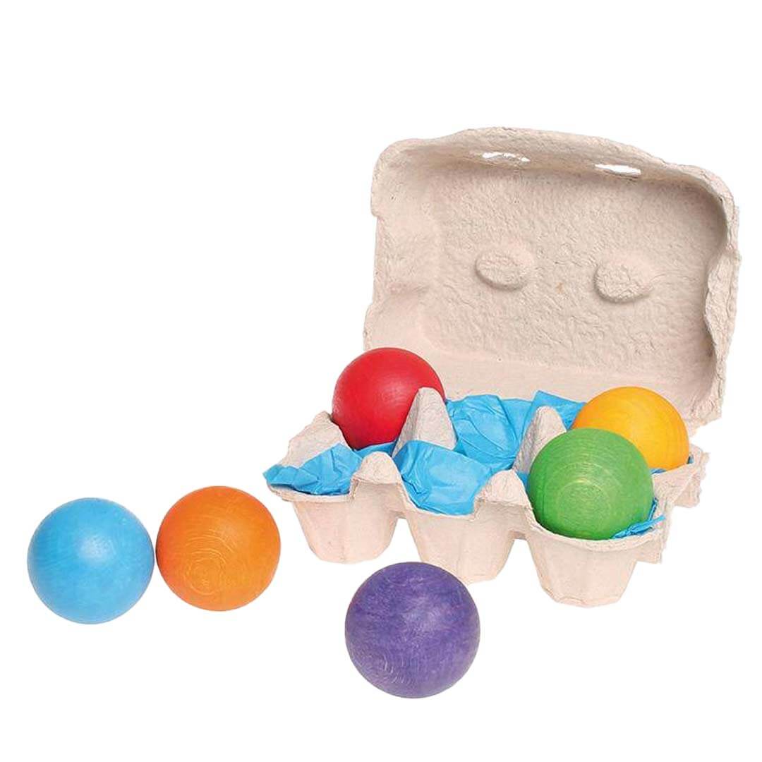 Colorful wooden balls in an open cardboard egg carton on a white background.