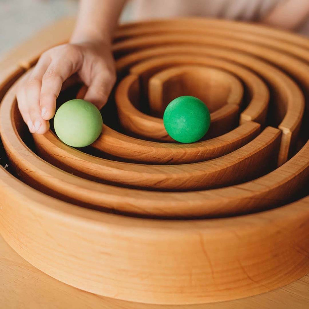 Wooden tunnel with green balls and a hand interacting with it.