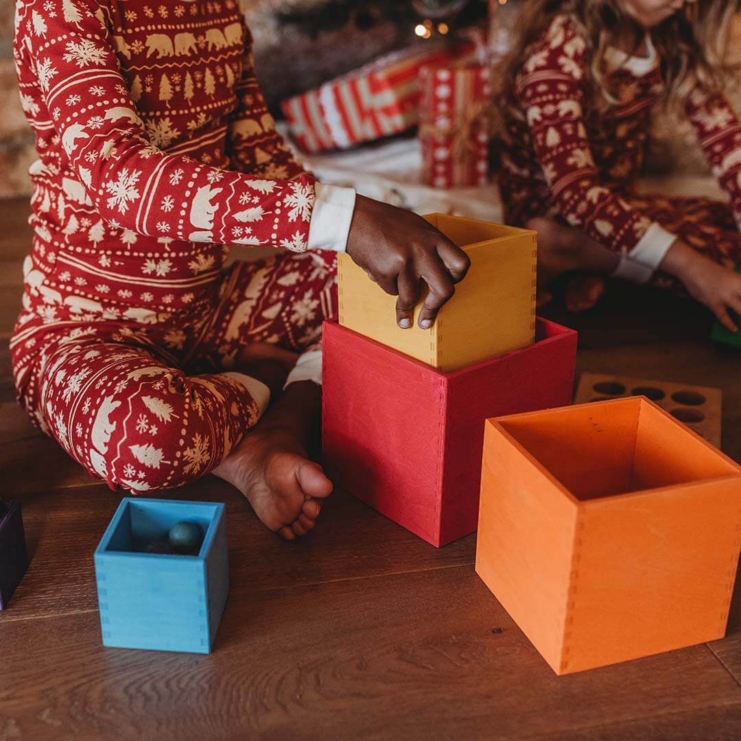 Person in festive pajamas interacting with colorful wooden blocks on a wooden floor.
