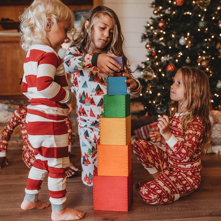 Three children playing with colorful blocks in front of a Christmas tree.