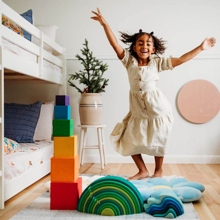 Child in a room with colorful blocks and a rainbow pillow.