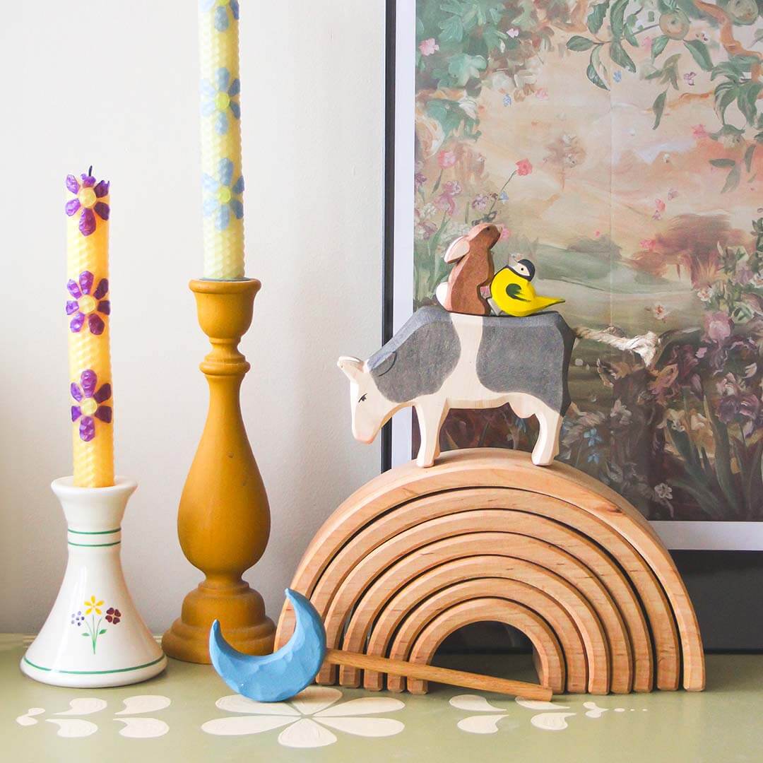Decorative items including a wooden rainbow, animal figurines, and candles on a surface.
