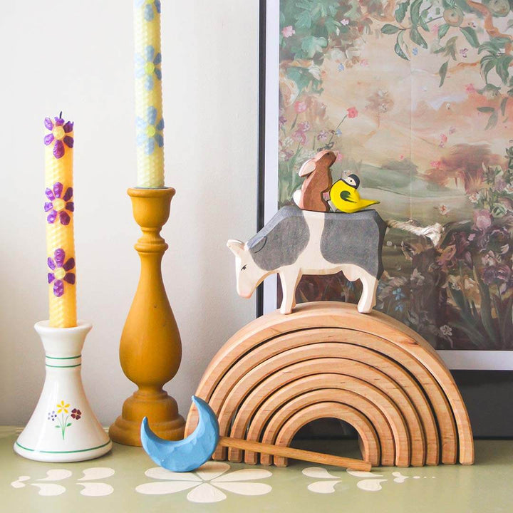Decorative items including a wooden rainbow, animal figurines, and candles on a surface.