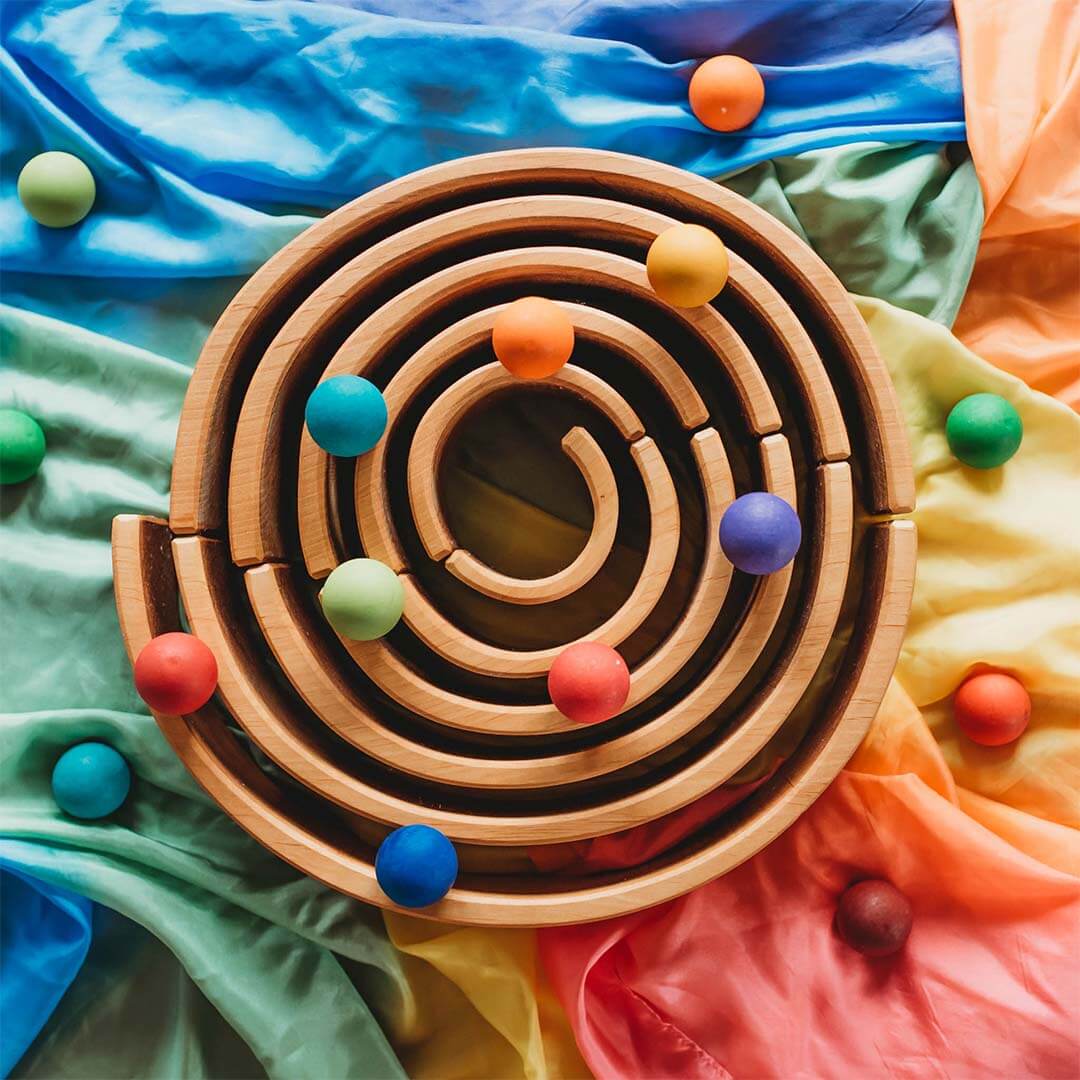 Wooden tunnel with colorful balls on a multicolored fabric background.