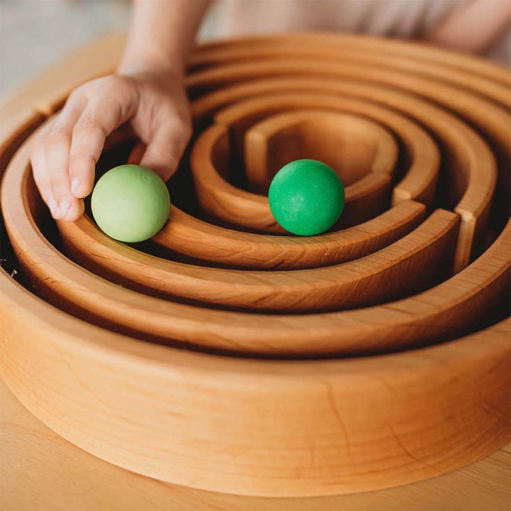 Wooden tunnel with green balls and a hand interacting with it.