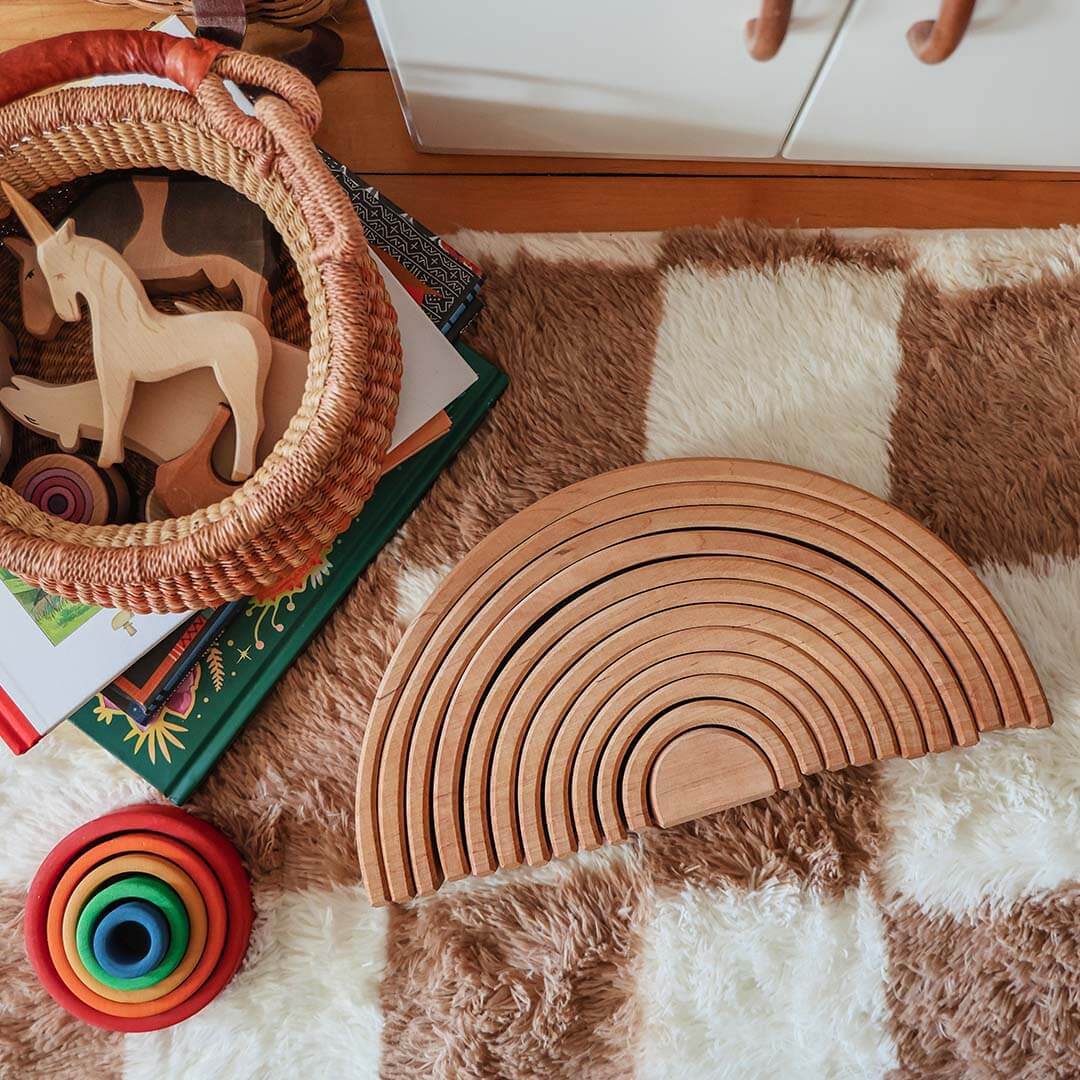 Wooden toys including a rainbow ring and animal shapes on a checkered rug.