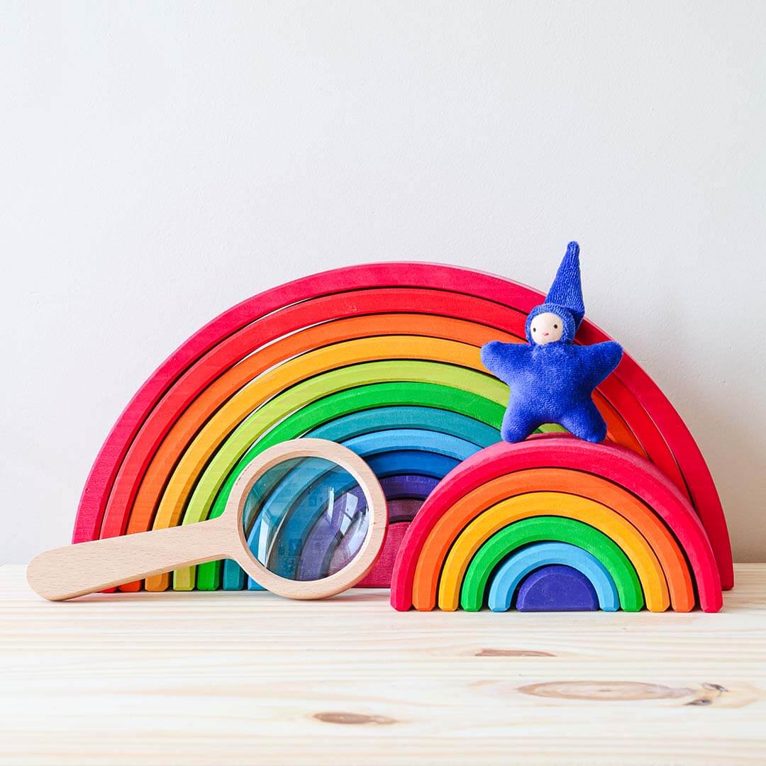 Colorful wooden rainbow toy with a blue star-shaped figure and magnifying glass on a light background.
