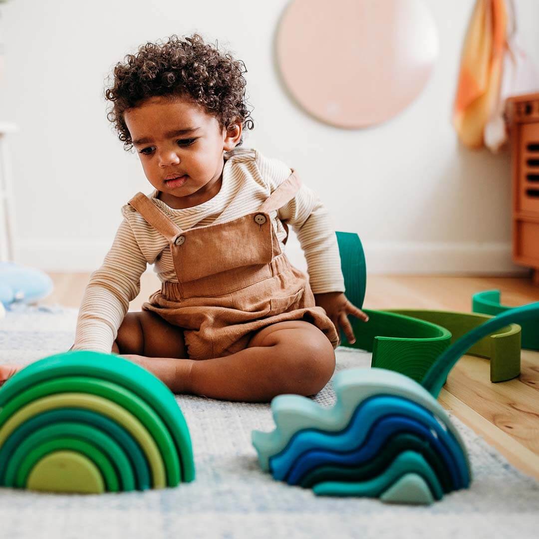 Child playing with colorful wooden toys on a wooden floor.
