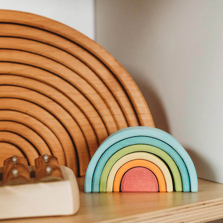 Wooden rainbow toy and circular wooden structure on a neutral background