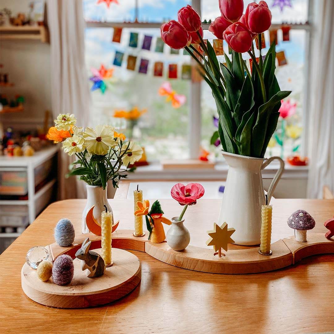 Decorative table setting with flowers, candles, and small figurines in a bright room.