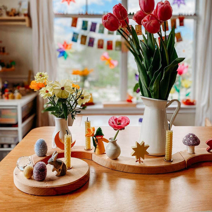 Decorative table setting with flowers, candles, and small figurines in a bright room.