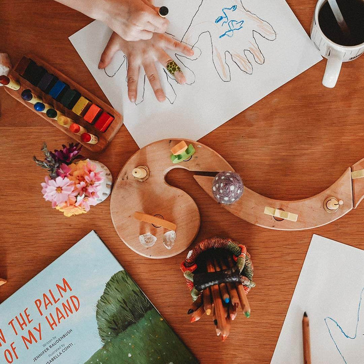 Artistic setup with watercolors, a book titled 'The Palm of My Hand', and a child's handprint on paper.