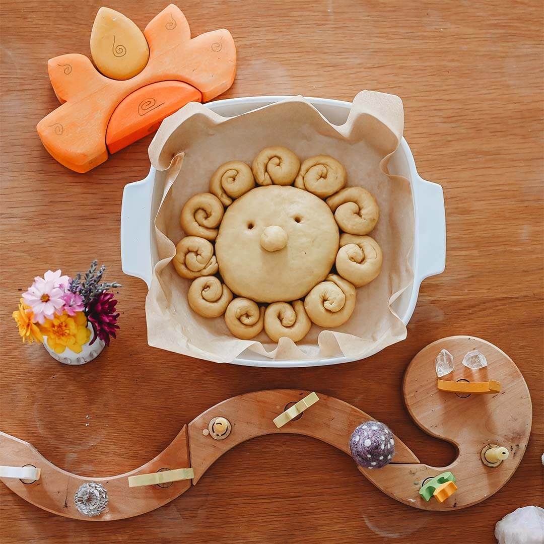 Sun-shaped bread in a baking dish on a wooden table with decorative elements.
