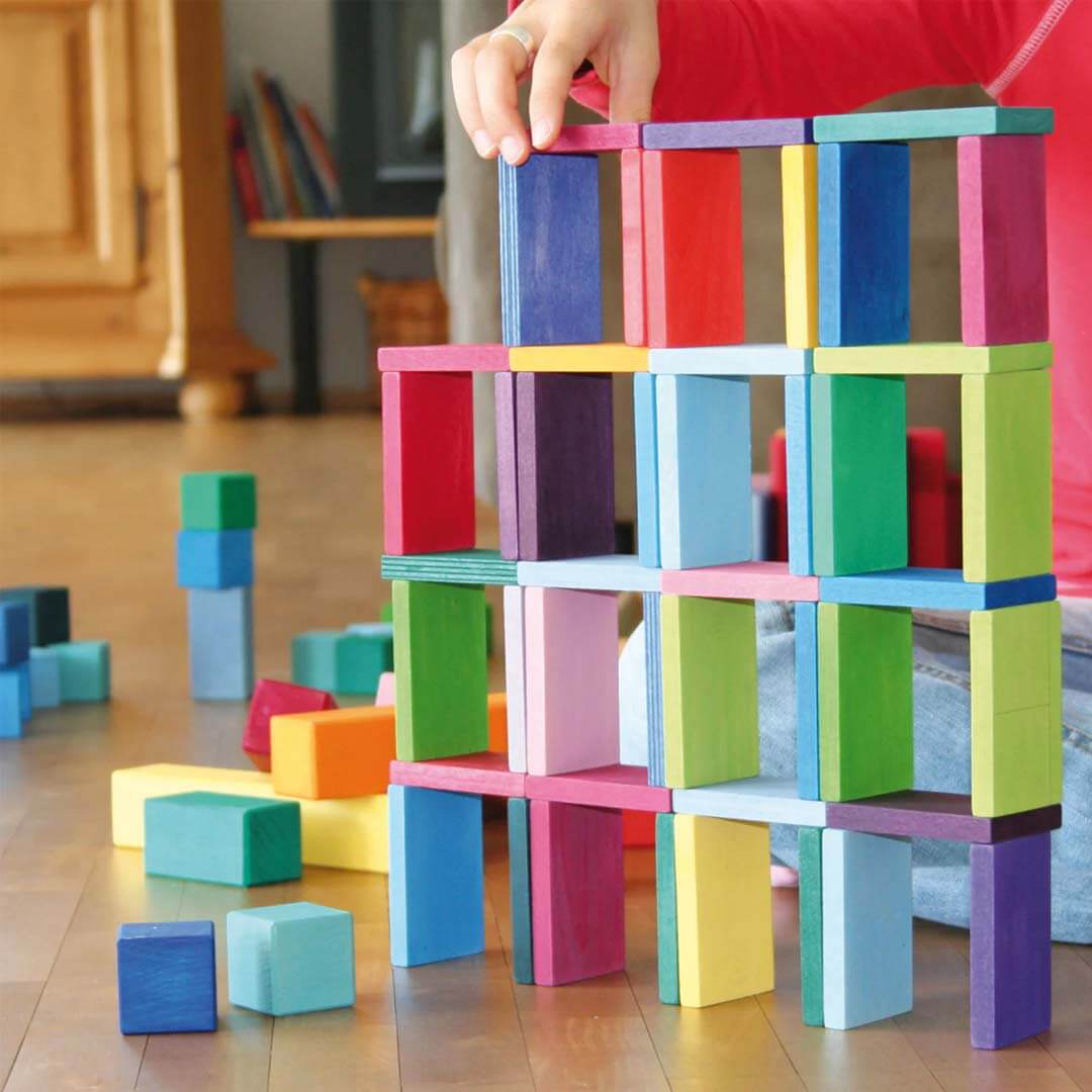 Colorful building blocks being held by a hand on a wooden floor.