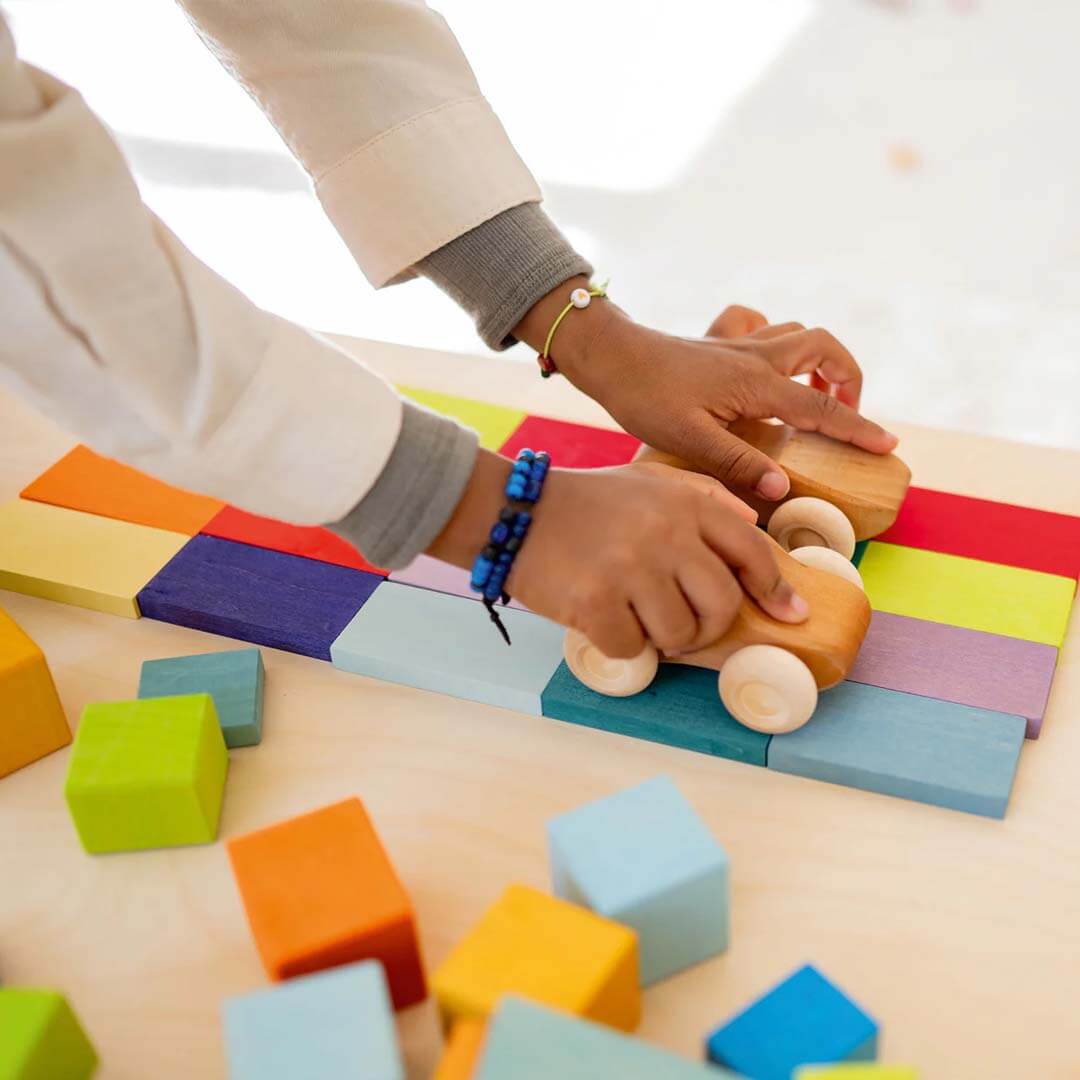 Child playing with colorful wooden blocks on a light surface.