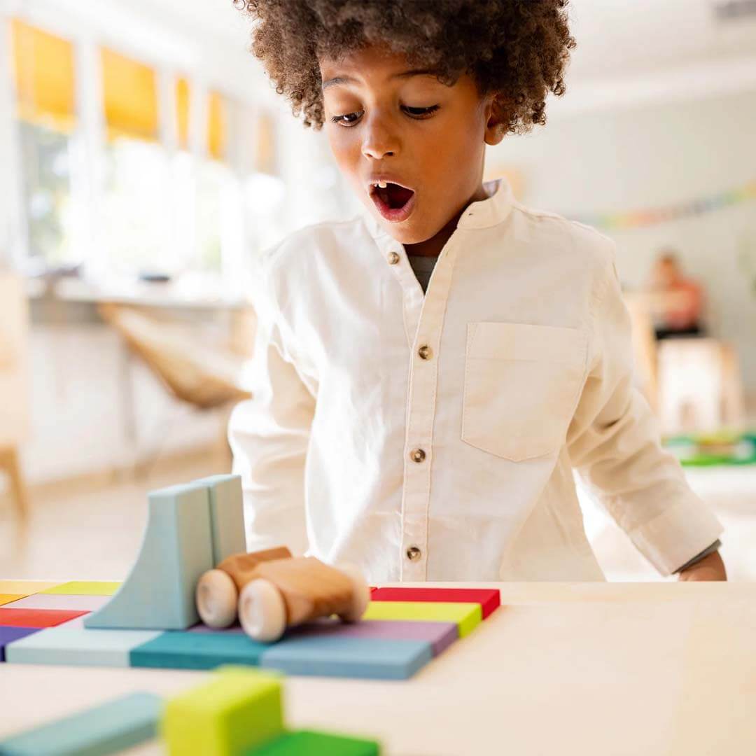Child playing with colorful wooden toys in a classroom setting.