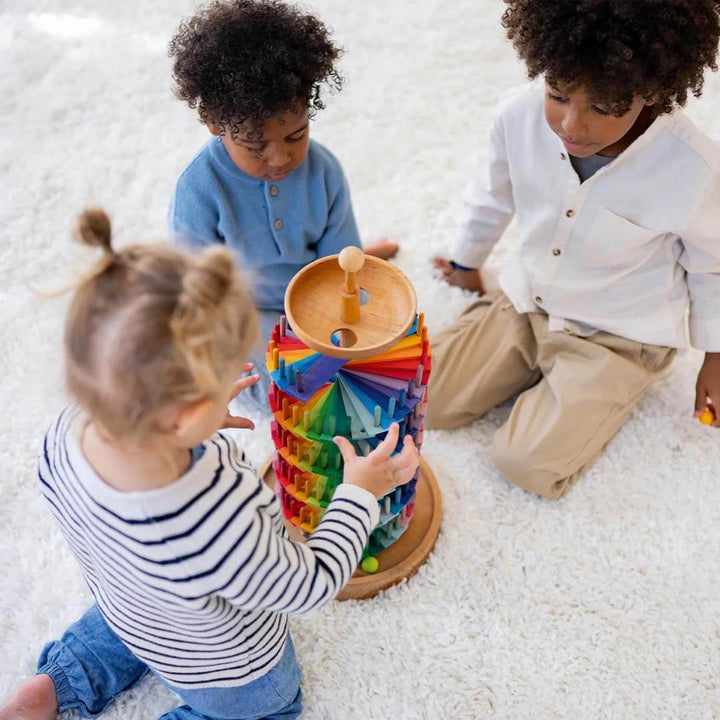 Three children playing with a colorful wooden toy on a white carpet.