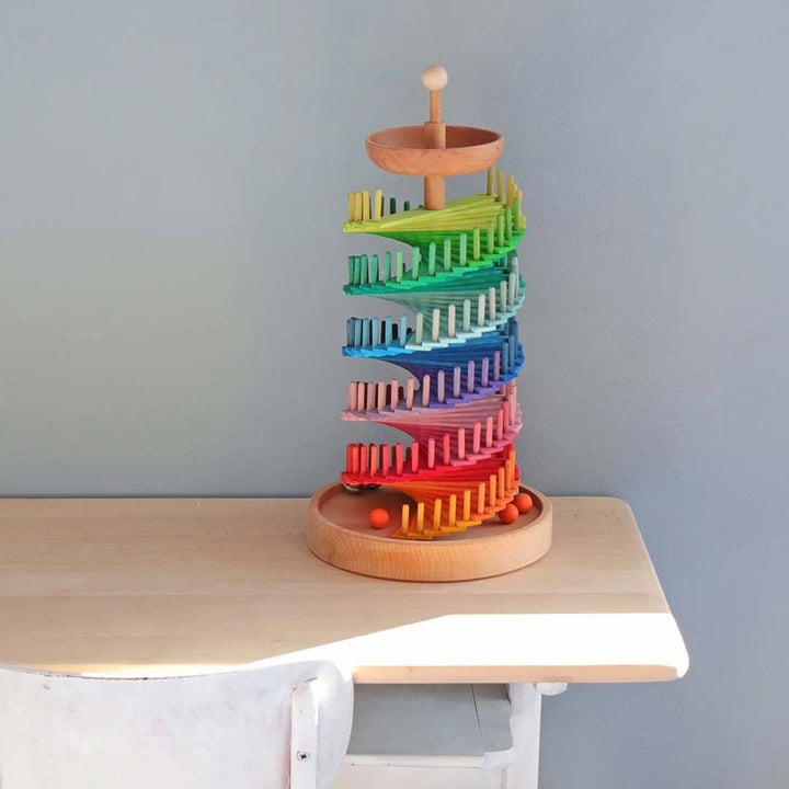 Colorful wooden toy with multiple levels on a light wooden surface against a gray wall.