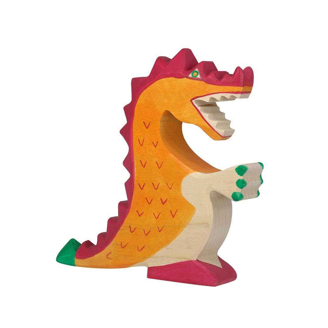 A handcrafted wooden toy dinosaur with a bright orange body, magenta-pink spikes along its back and head, a natural light wood underside, green claws on its front paw, and a green tail tip, set against a plain white background.