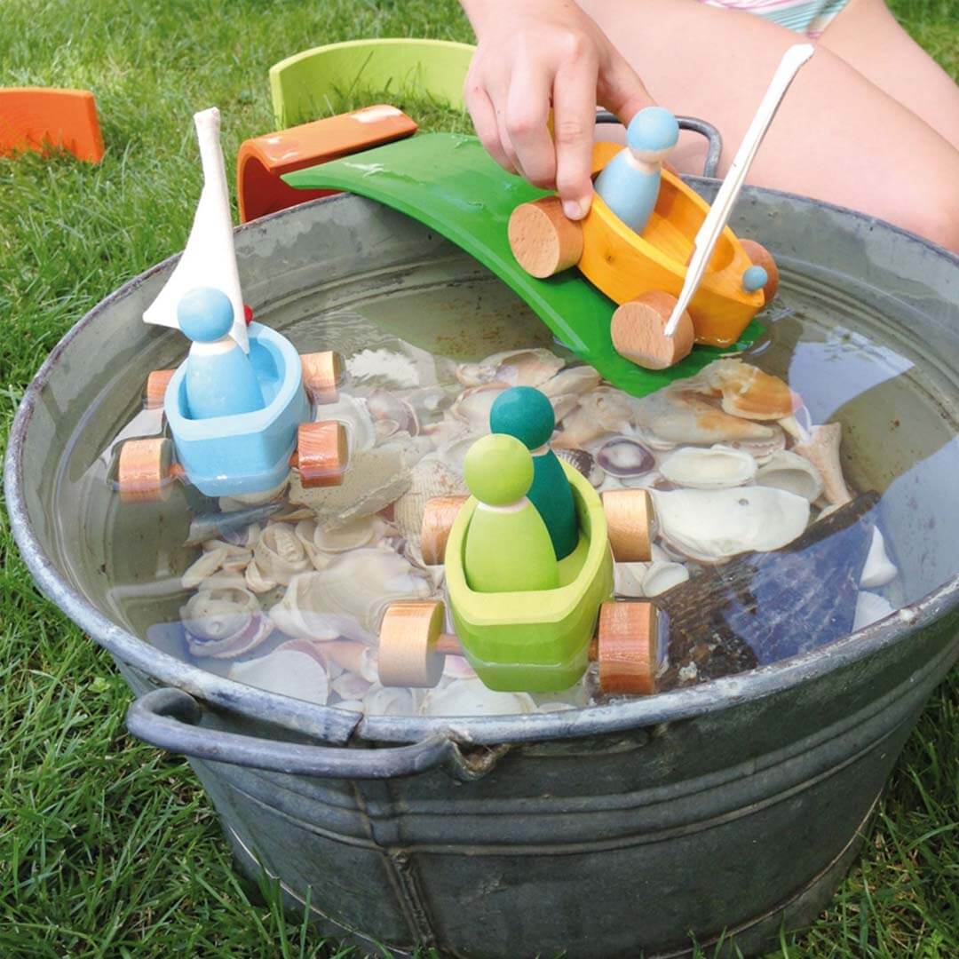 Children's toy boats in a bucket filled with water and shells on a grassy background