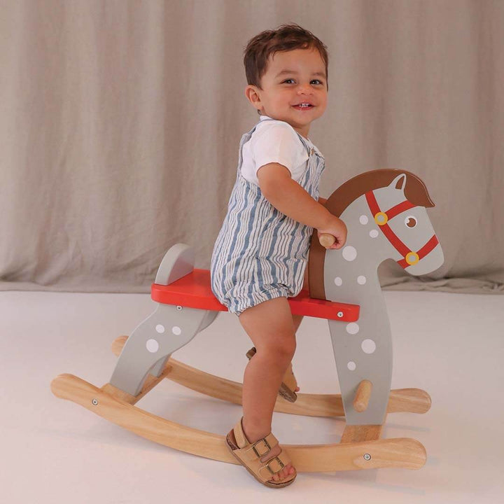 Child riding a wooden rocking horse with a plain background