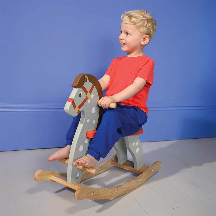 Child sitting on a wooden rocking horse against a blue wall