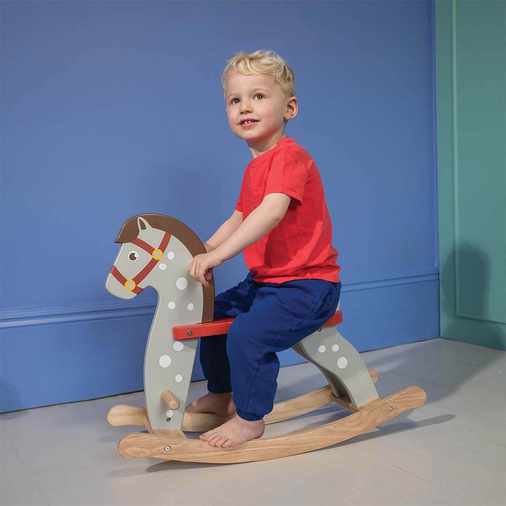 Child riding a wooden rocking horse against a blue wall