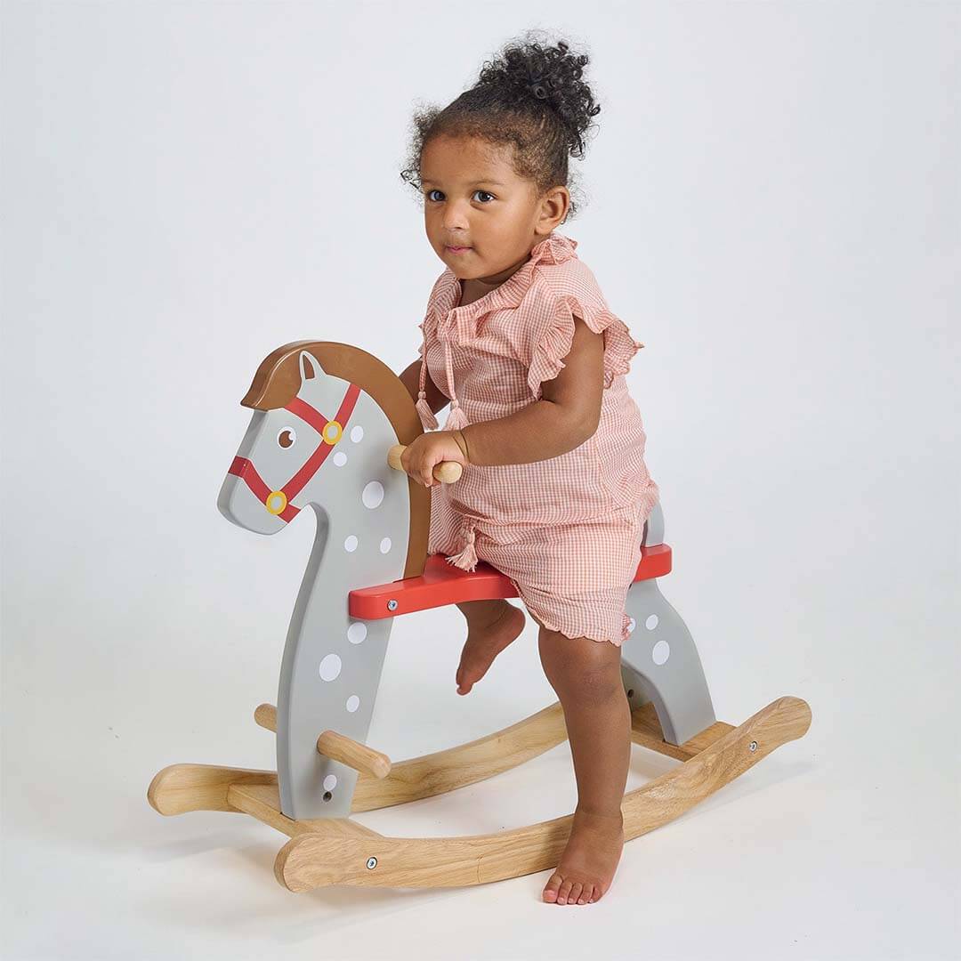Child sitting on a wooden rocking horse against a plain background