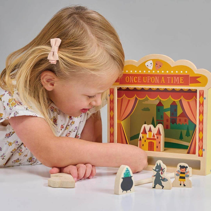 Child playing with wooden storybook characters in front of a 'Once Upon a Time' puppet theater.